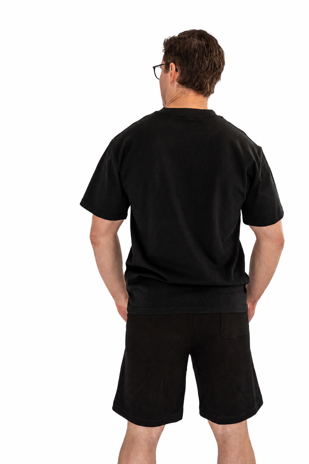A man viewed from behind wearing a plain black short-sleeve t-shirt and black shorts against a solid white background.