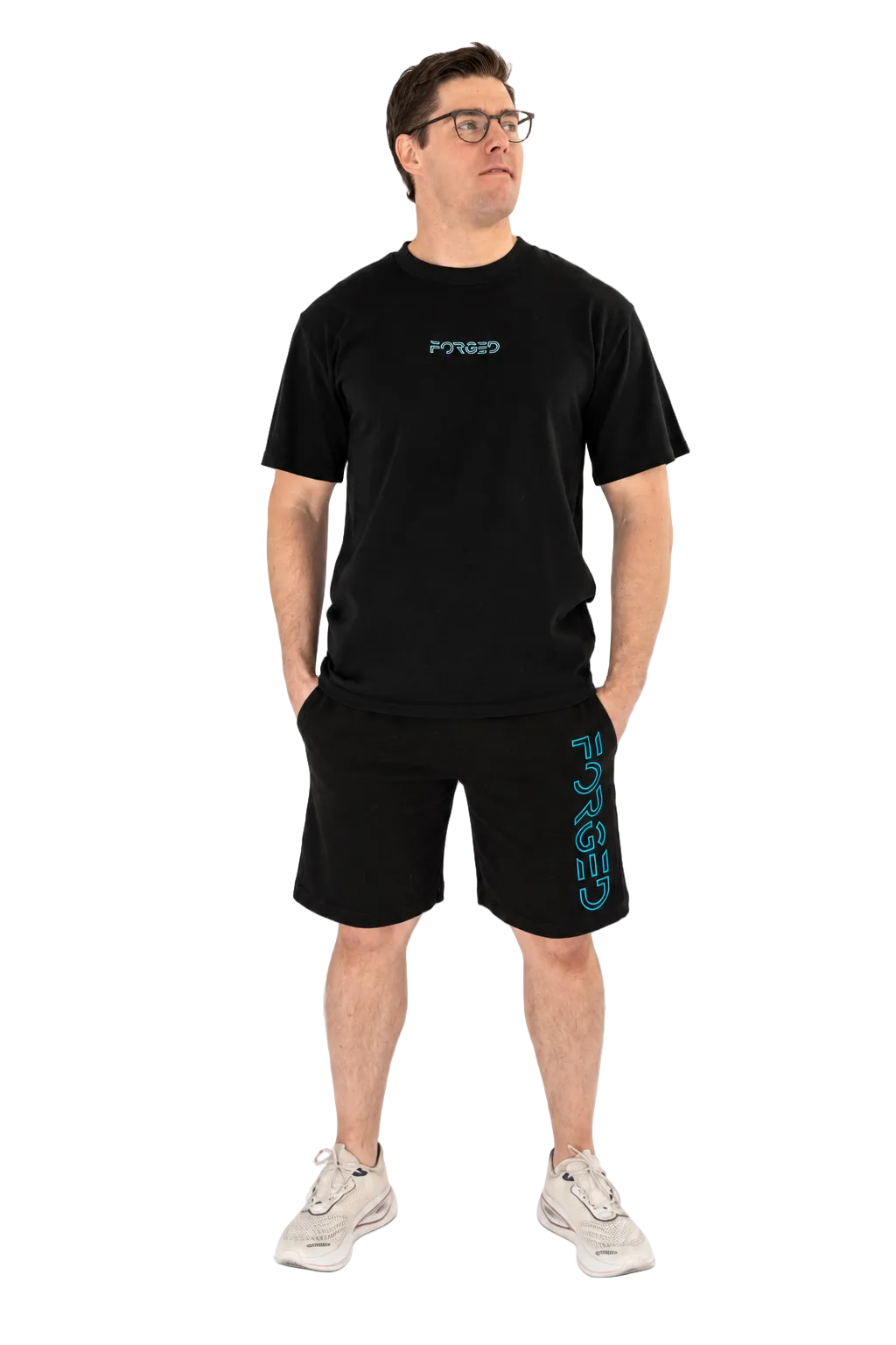 A man wearing a black short-sleeve t-shirt and matching black shorts with teal graphics, standing against a plain white studio background.