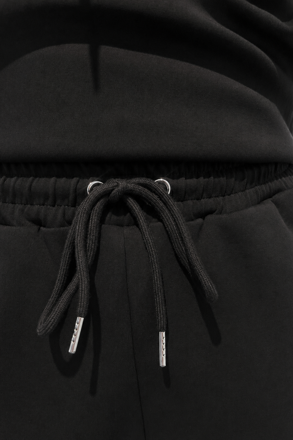 Close-up of a black hooded sweatshirt or sweatpants with a drawstring waist, showing the drawstring cords and metal eyelets against dark fabric.