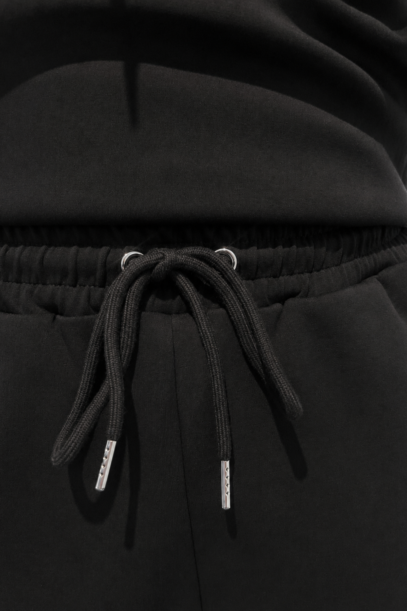 Close-up of a black hooded sweatshirt or sweatpants with a drawstring waist, showing the drawstring cords and metal eyelets against dark fabric.