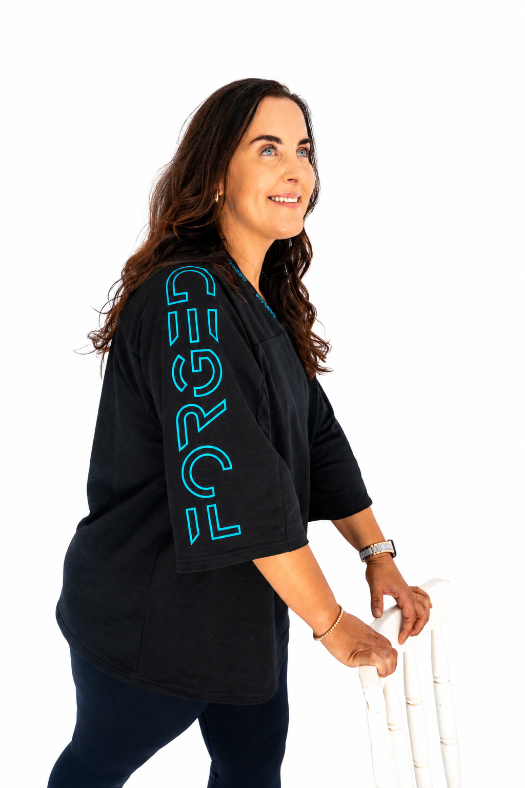 A woman wearing a black short-sleeve t-shirt with 'FORGED' printed vertically in bright blue on the sleeve, holding a white paddle on a solid white background.