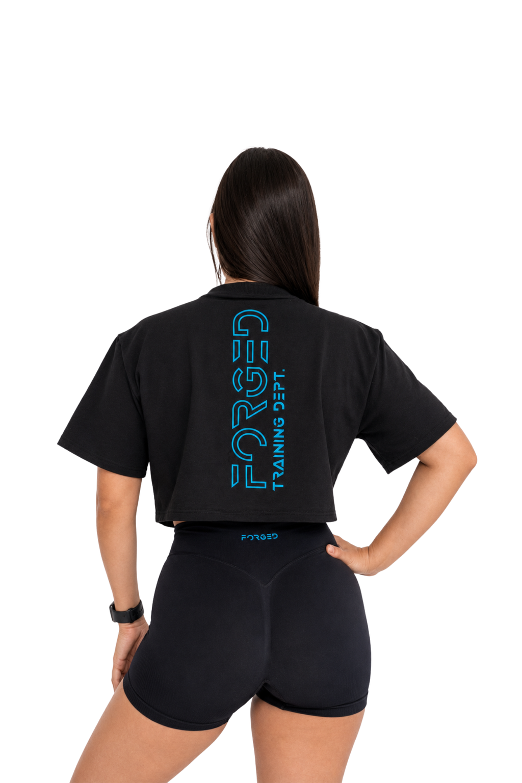 A woman shown from the back wearing a black short-sleeve crop top and matching black shorts. The back of the top features a large vertical blue graphic reading 'FORGED TRAINING DEPT.