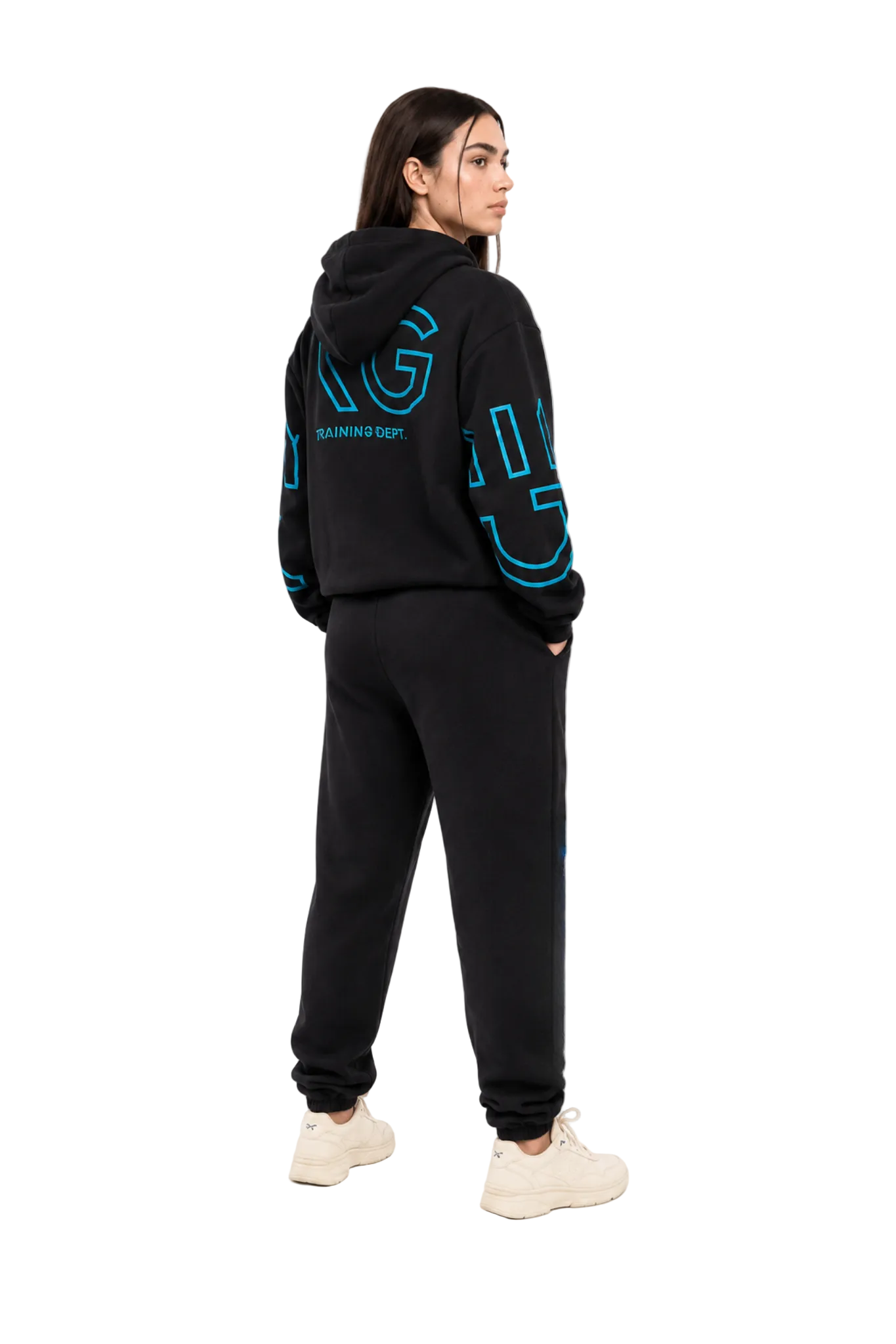 A woman shown from the back wearing a black hooded sweatshirt and matching black jogger pants with bright blue outlined lettering on the back and sleeves, paired with off-white sneakers, against a plain white studio background.