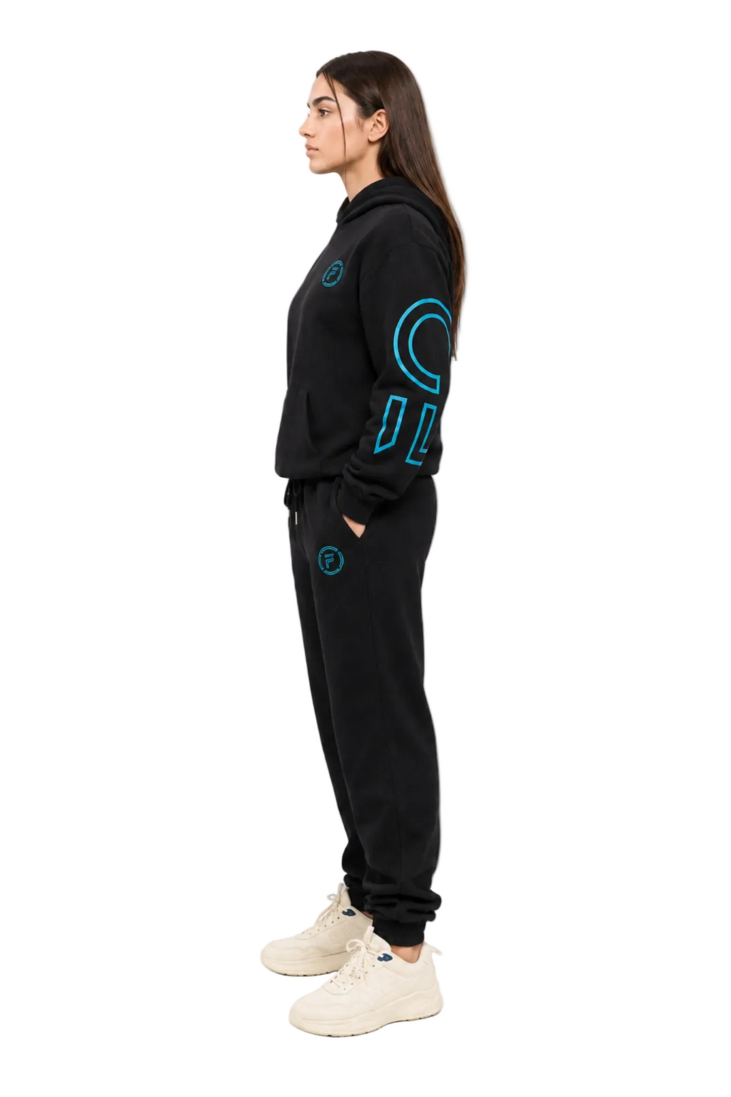 A woman in profile wearing a black tracksuit with bright blue graphic details on the sleeves and pants, paired with off-white sneakers, against a plain white background.
