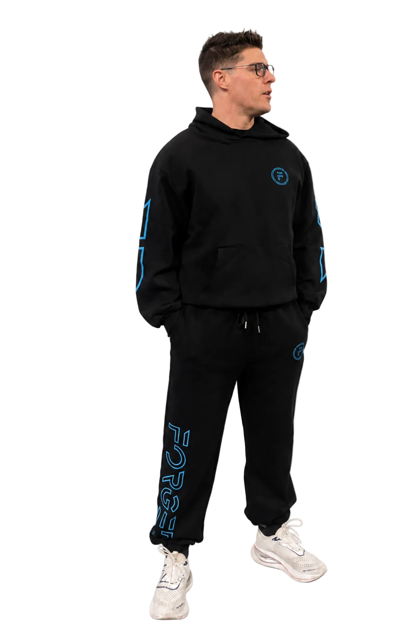 A man wearing a black hooded sweatshirt and matching sweatpants with bright blue graphic details, standing against a plain white studio background.