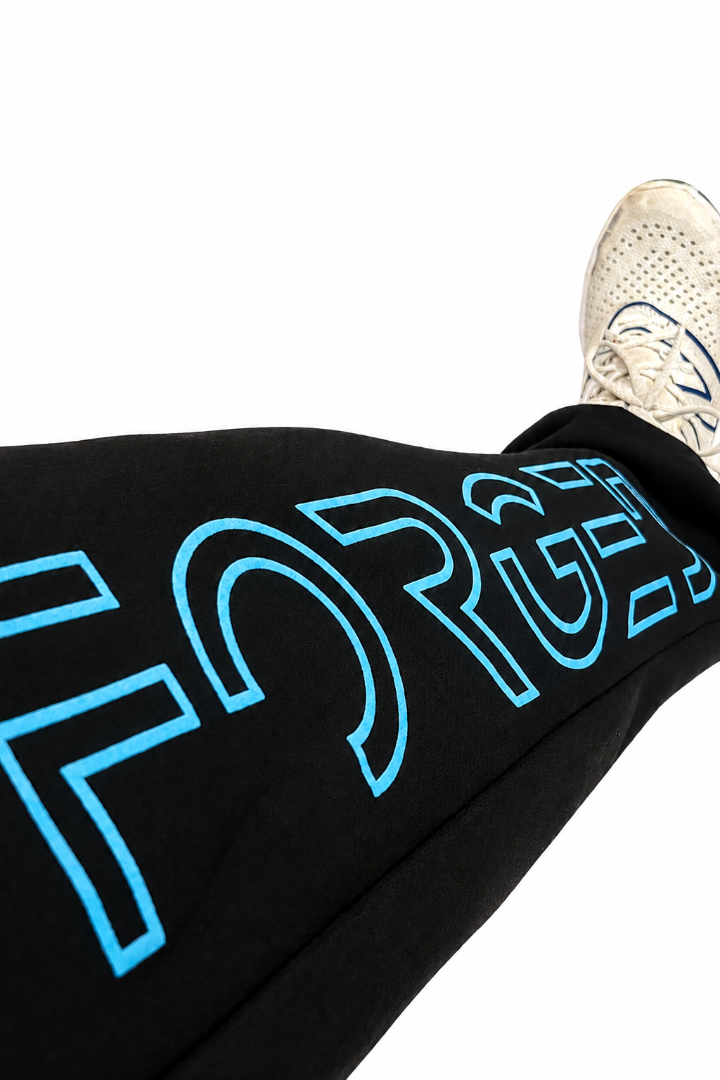 Black sweatpants with a large light blue outline graphic spelling 'FORGED' across the leg, shown on a person wearing white sneakers against a plain white background.