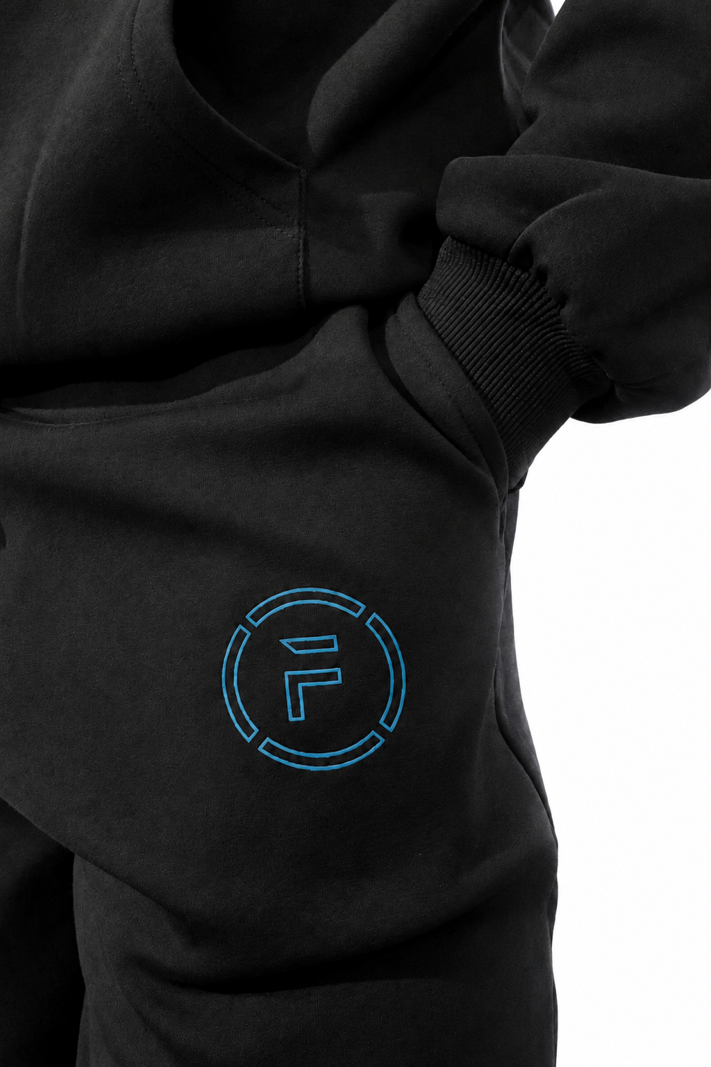 Close-up of a black hoodie with a light blue circular 'F' logo on the chest, showing the sleeve cuff and fabric texture.