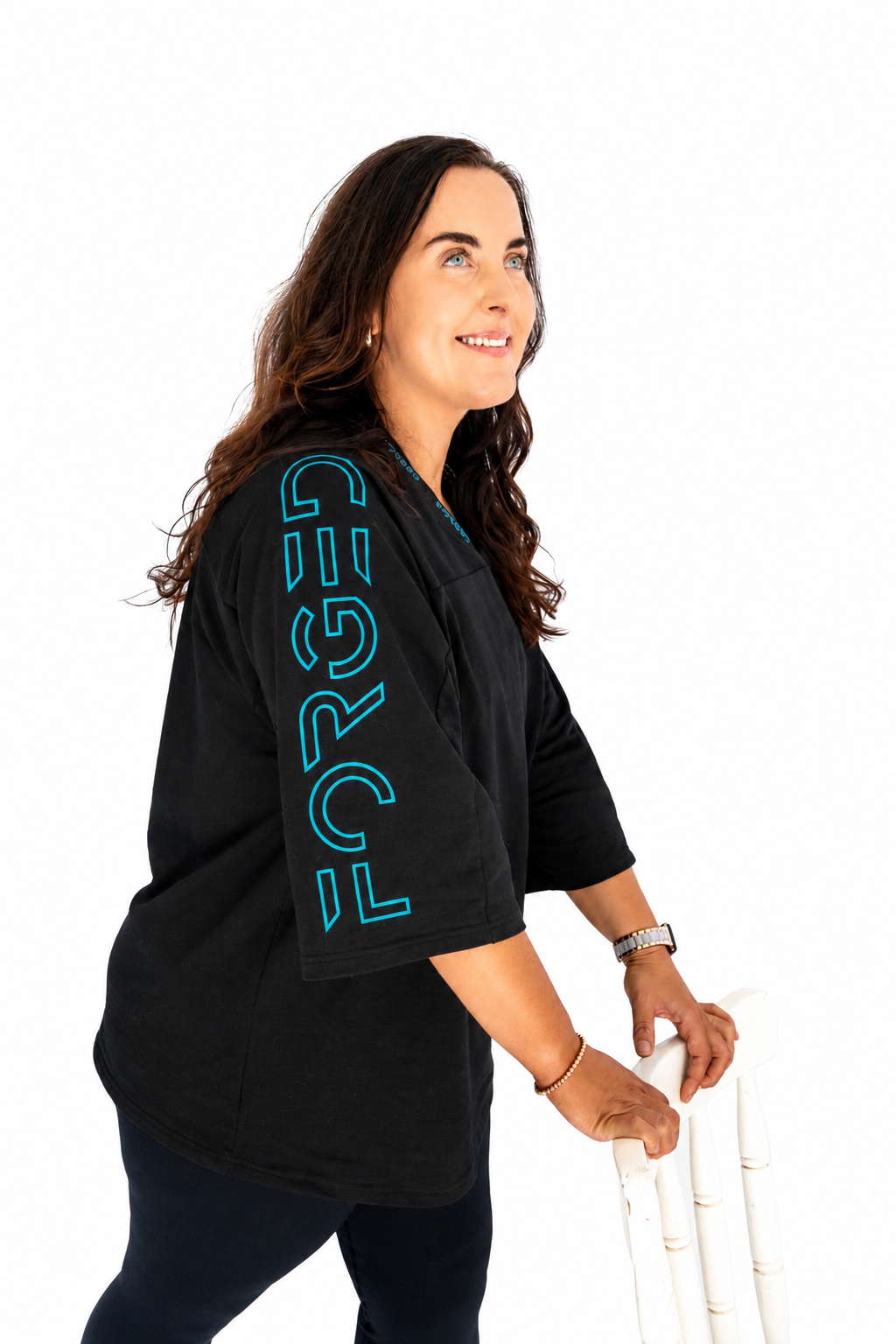 A woman wearing a black oversized t-shirt with a bright blue vertical 'FORGED' graphic on the sleeve, holding a white pole against a solid white background.