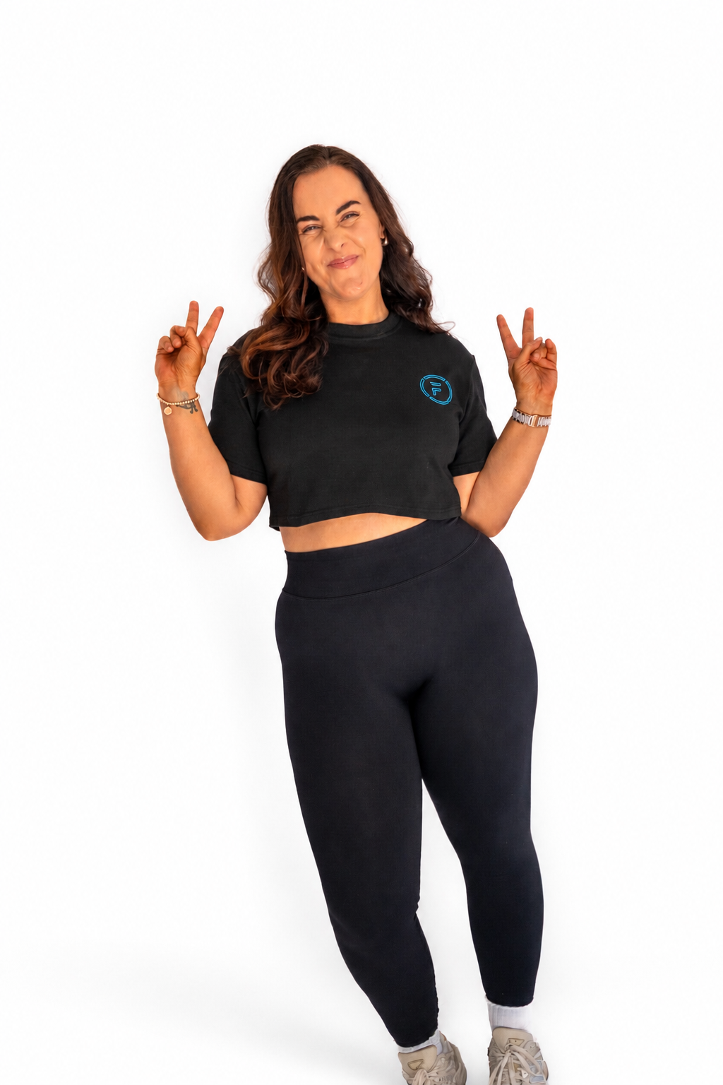 A woman modeling a black short-sleeve crop top and matching black leggings against a plain white background.