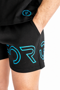 Close-up of a person wearing black athletic shorts with large bright blue outlined lettering on the side and a matching blue circular logo on the shorts top, photographed against a white background.
