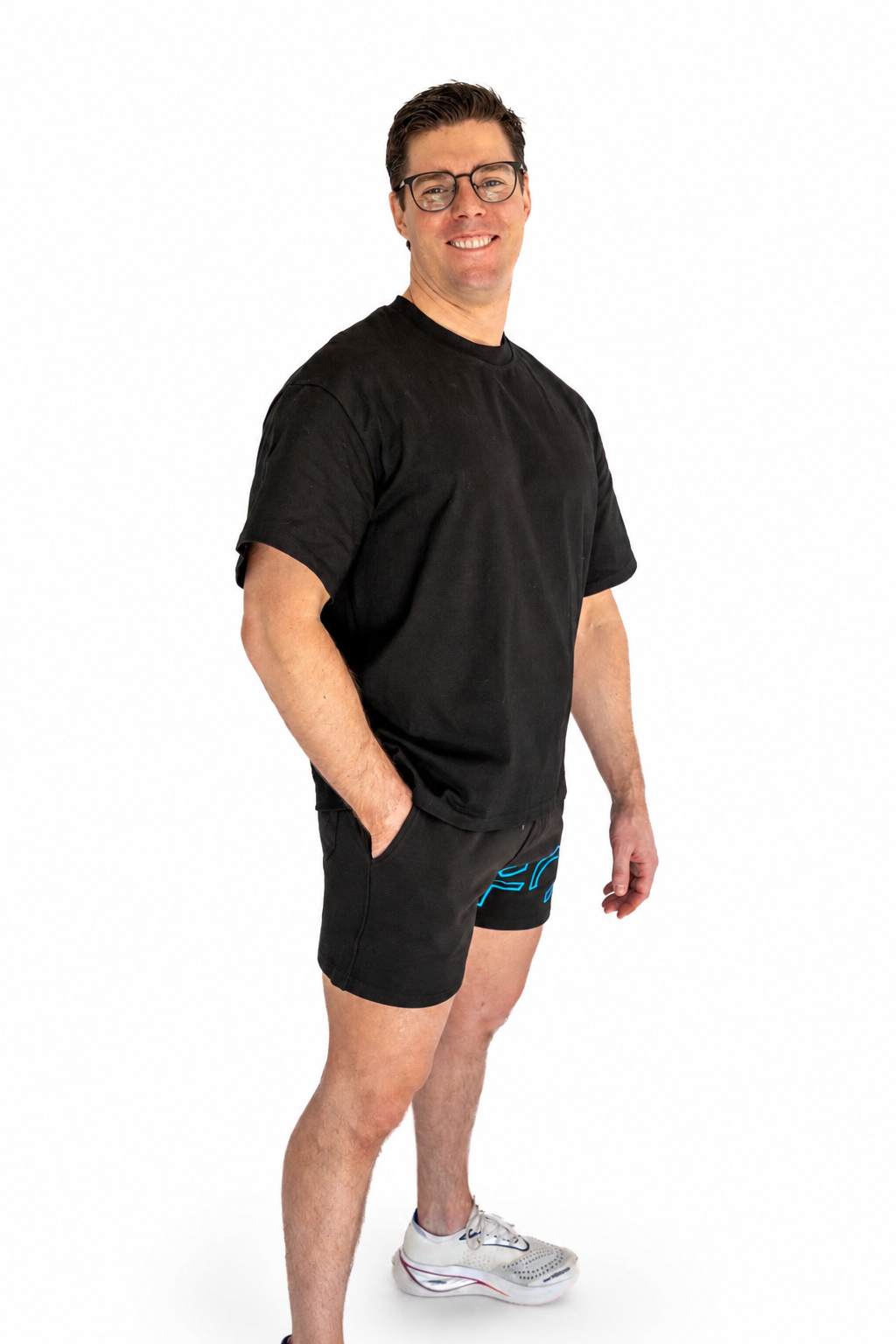 A man wearing a black crewneck t-shirt and black athletic shorts with a blue graphic detail, standing against a solid white background.