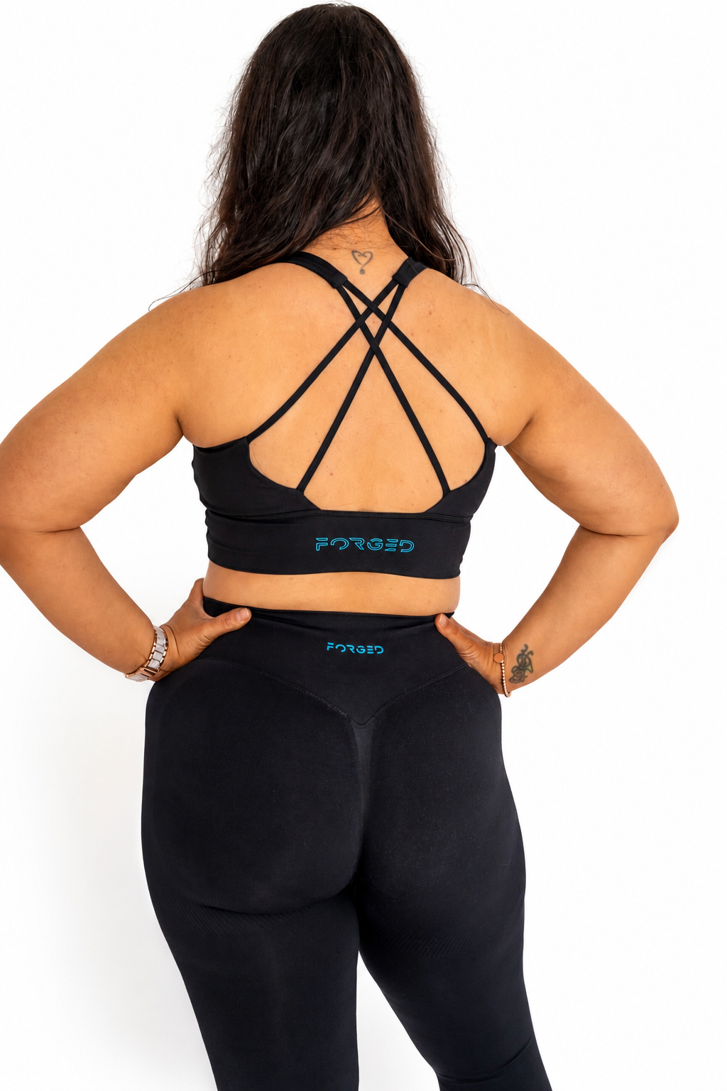 A woman shown from the back wearing a black sports bra and matching black leggings with a teal 'FORGED' logo on the waistbands, against a plain white background.