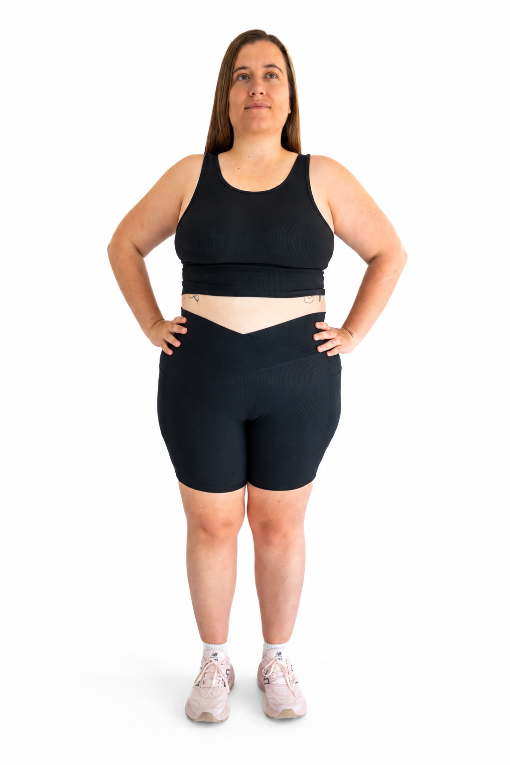 A woman modeling a black athletic set consisting of a cropped tank top and matching fitted shorts, standing against a plain white background.